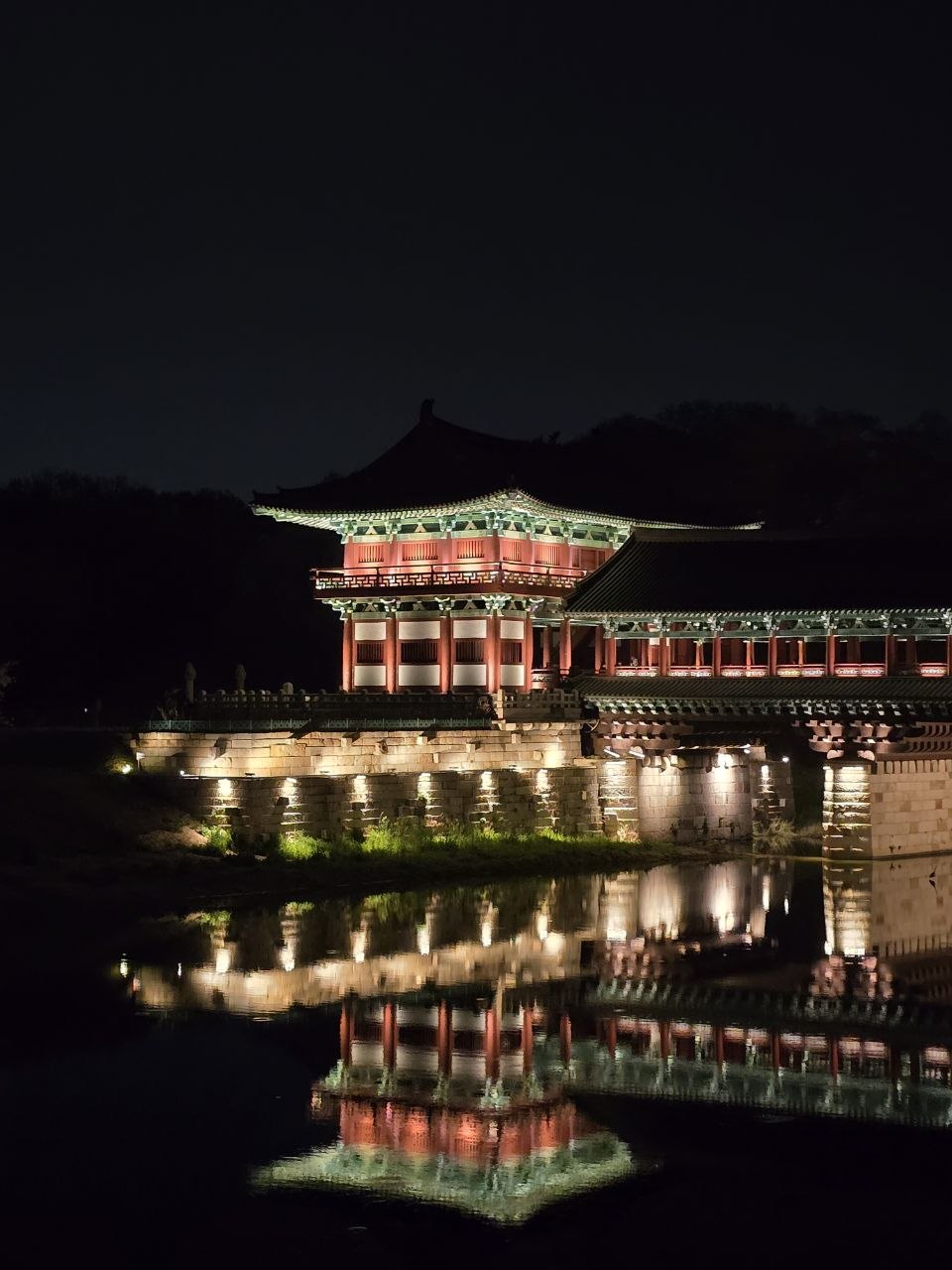 A pavilion at night, reflected in still water — House of Choi.